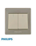 Philips two-switch light switch plate in a warm beige finish with a matching metallic frame, shown on a white background with a blue Philips logo watermark at the bottom left.Supplied by Chinoy Electric